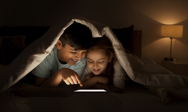 Siblings reading on an ereader in the dark in bed