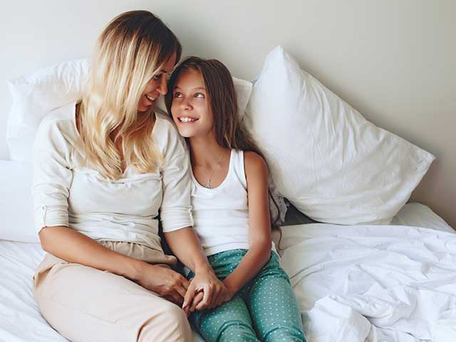 Mother and daughter holding hands sitting up in a bed